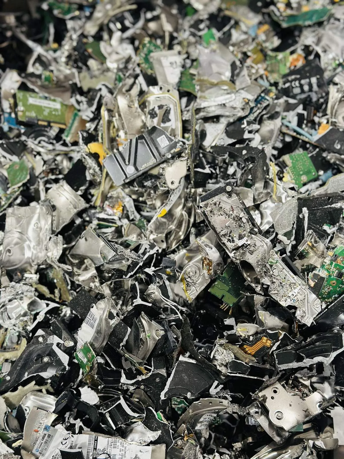 A pile of hard drives after shredding: torn aluminum housings, platters, and green circuit boards