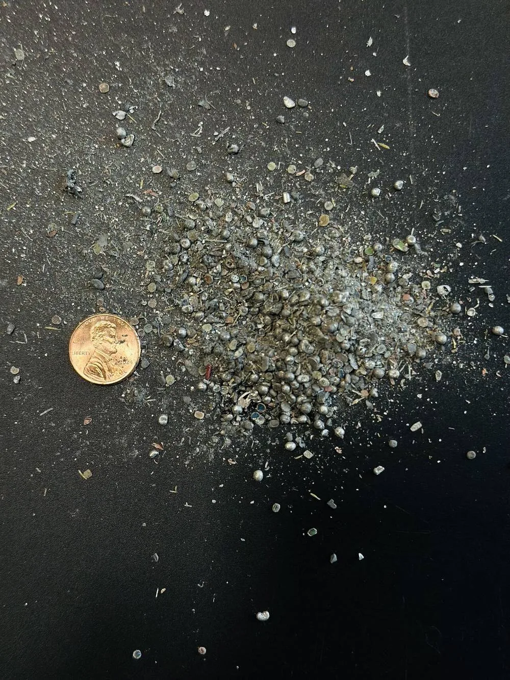 A small pile of grey metallic particles next to a penny for scale